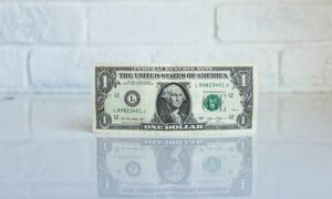 Image of a 1 Dollar bill from America against a white brick background demonstrating dollar FATCA fees in Portugal | GetNif