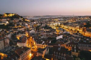 Image of Lisbon at dusk showing buildings with golden lights emitting, Americans moving to Portugal | GetNif