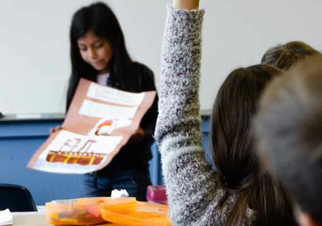 Image of child showing her work in an international school classroom, child with hand raised blurred in the foreground of the image, International schools in Portugal | GetNif