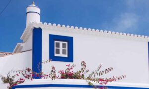 White and blue Portuguese home with chimney and pink flowers growing over the wall, blue and white small window on side of house, Stamp Duty Portugal | GetNif